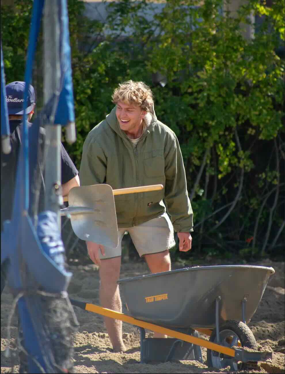 Photo of a man working outdoors with a wheelbarrow. 