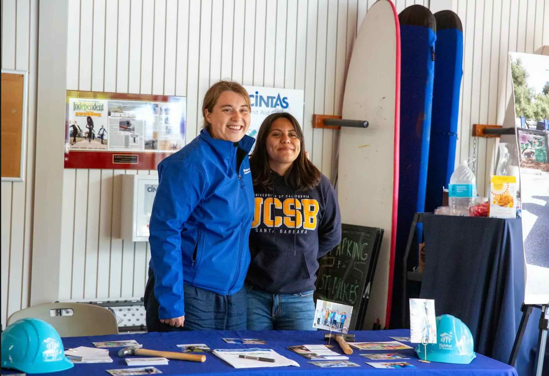 Photo of two young women smiling for a picture while tabling. 