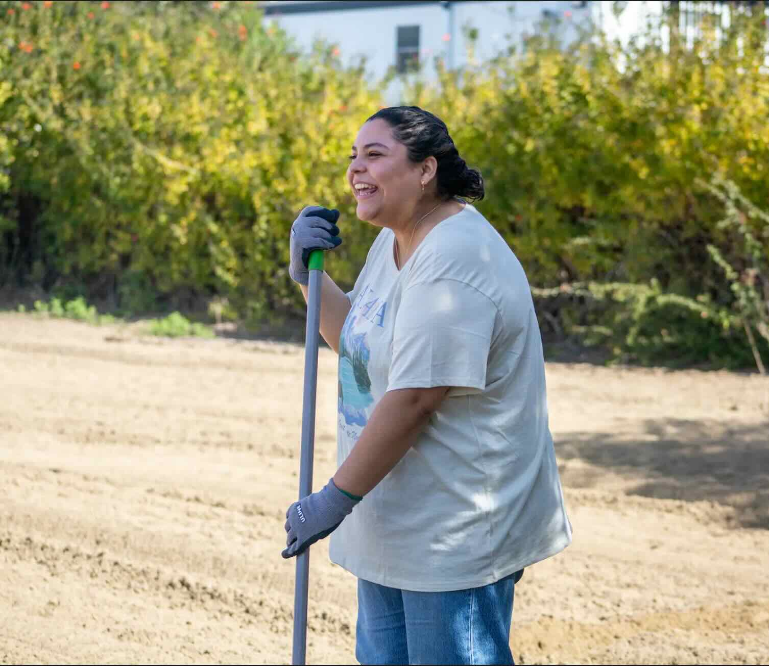 Photo of a young woman smiling while holding a gardening tool 